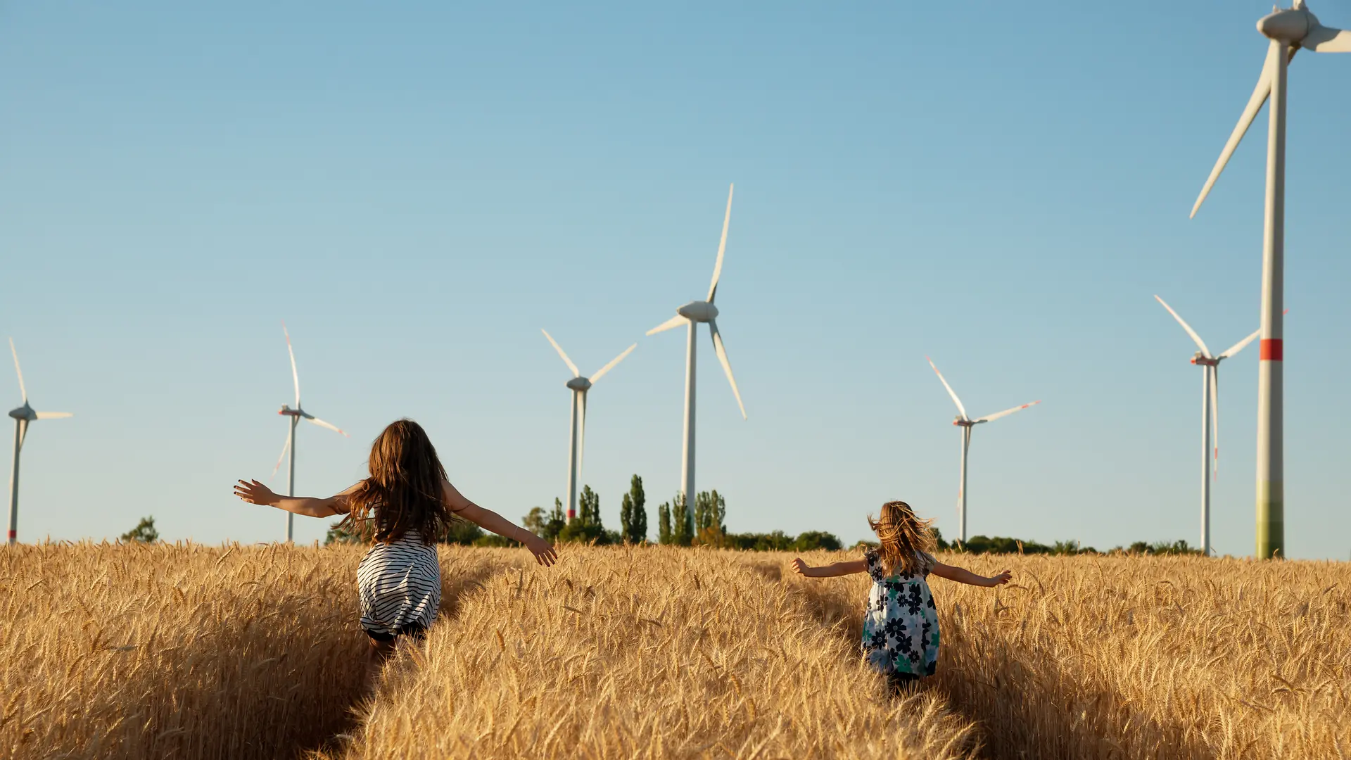 Bambine che corrono in un campo con pale eoliche