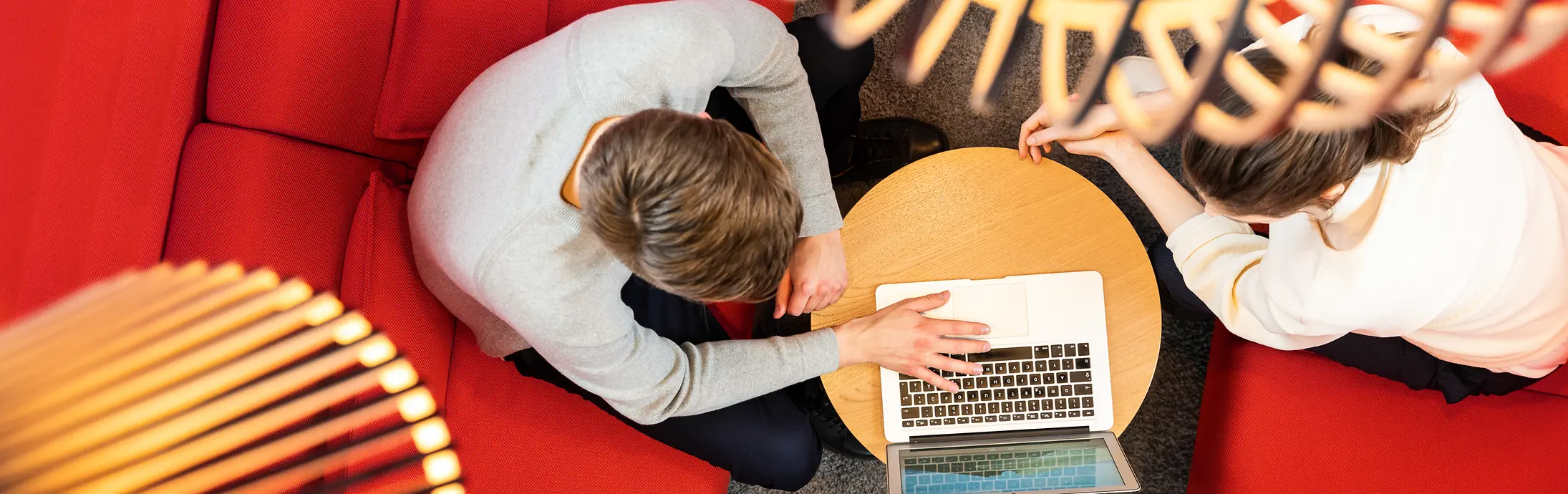 Due persone al lavoro con un laptop sedute su un divano rosso