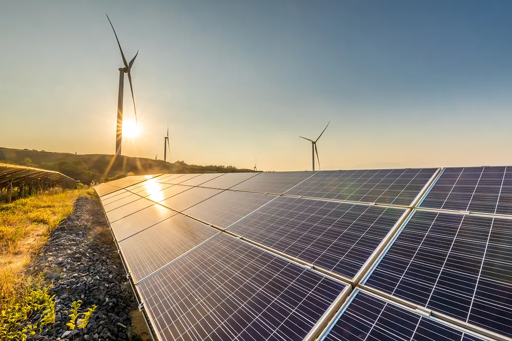 Pannelli solari al tramonto con turbine eoliche sullo sfondo