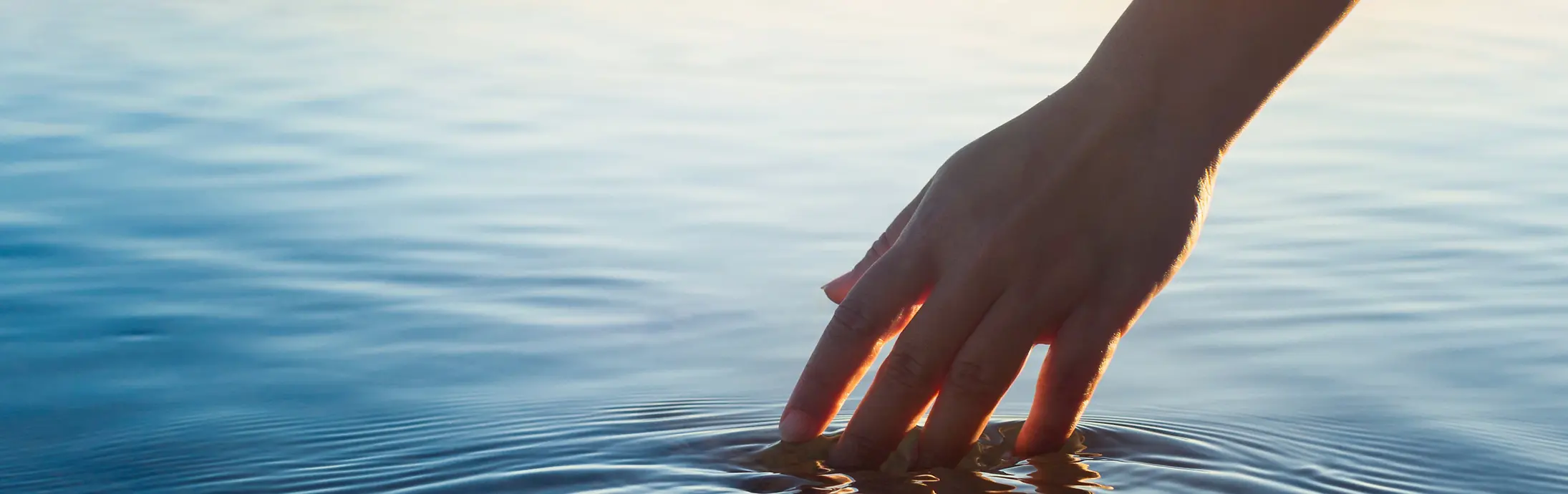 Una mano accarezza una piatta superficie d'acqua al cospetto dell'orizzonte