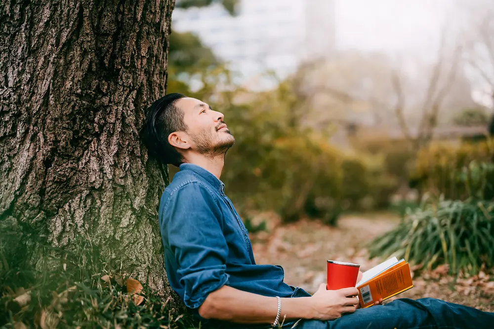 Uomo con in mano un libro appoggiato a un albero