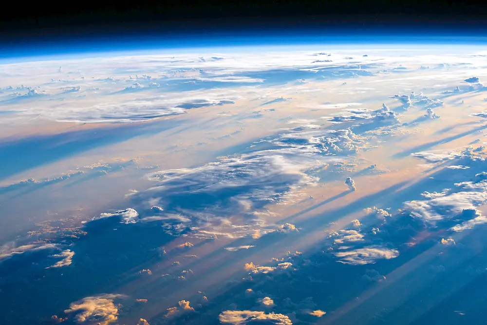 Blick von der ISS über das Philippinische Meer, mit tiefblauem Ozean, vereinzelten Wolken und dem gekrümmten Horizont der Erde vor dem schwarzen Weltraum.